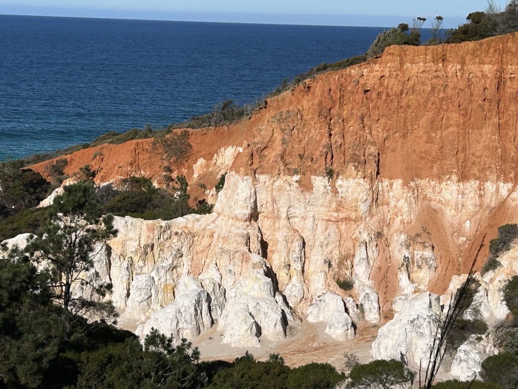 Sunlit cliff face in Eden, NSW showing layered earth and rock, symbolising the journey from surface noise into deep inner stillness where spiritual transformation and gemstone like clarity are formed.