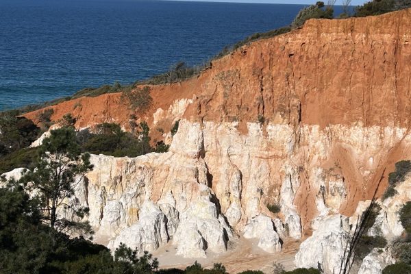 Sunlit cliff face in Eden, NSW showing layered earth and rock, symbolising the journey from surface noise into deep inner stillness where spiritual transformation and gemstone like clarity are formed.
